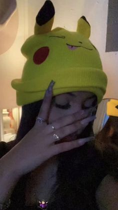 a woman in a pikachu hat covers her face with her hands while looking at the camera