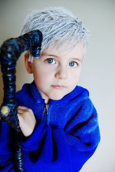 a young boy with grey hair and blue eyes holding a black object in his hand