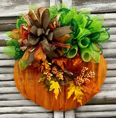 an orange pumpkin decorated with green and yellow leaves on a wooden background, hanging from the side of a building