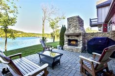 an outdoor patio with chairs, table and fire place in front of a lake view