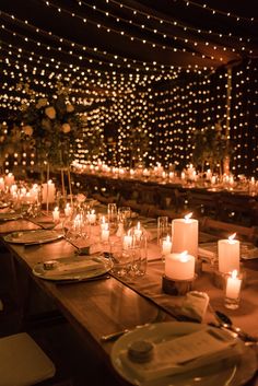 a long table is set with candles and place settings in front of a wall of lights