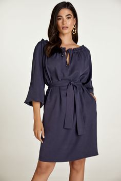 This belted dress is crafted in navy woven tencel fabric. It has a wide round neckline with an internal tie allowing either for ruching or an off-shoulder look. The tie is in the same fabric with metal stoppers at the ends. There is a V opening below the neckline. It has long raglan sleeves with elastic at the cuffs creating gathers. There is an inseam pocket on either side. The dress can be worn without the belt for a sack silhouette. The belt is included. 100% tencel  Gentle machine wash. Turn garment inside out. Cold water. Mild detergent. Iron on reverse side. Do not tumble dry. Do not bleach. Chic Blue Dress With Belted Cuffs, Elegant Midi Dress With Tie Fastening For Brunch, Elegant Brunch Dress With Belted Cuffs, Chic Off-shoulder Belted Dress, Inseam Pocket, Tencel Fabric, Artisan Gift, Gifts For New Mums, Blazer With Jeans