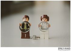 two legos are standing next to each other on a white surface, one is holding a watch and the other has a ring