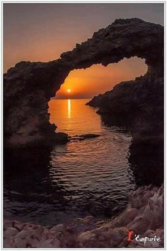 the sun is setting over the ocean through an arch shaped rock formation in the water