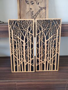 two wooden panels with trees cut out of them on top of a wood floor next to a painting