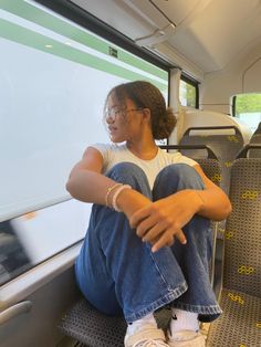 a woman sitting on the seat of a bus with her arms crossed and looking out the window