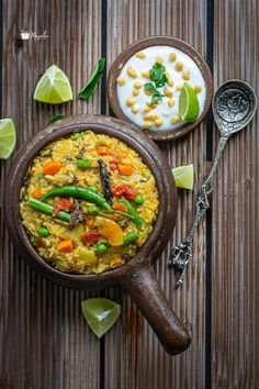 a wooden bowl filled with rice and vegetables next to two spoons on top of a table