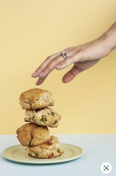 a hand reaching for a stack of food on top of a white plate next to a yellow wall