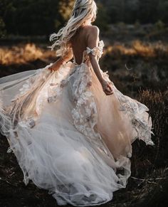 a woman in a wedding dress walking through the grass with her back to the camera