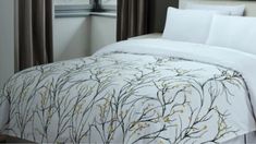 the comforter is white and has yellow flowers on it, along with brown drapes