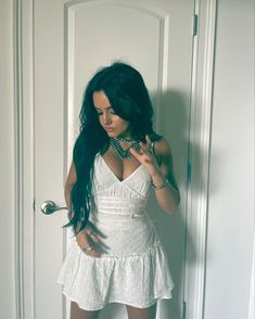 a woman standing in front of a door with her hands on her hips and wearing a white dress