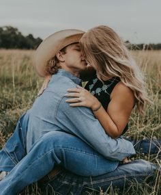 a man and woman sitting on the ground kissing each other in a field with tall grass