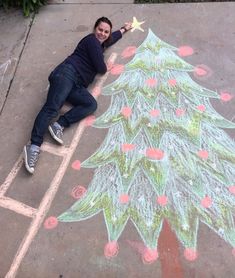 a woman laying on the ground next to a chalk drawing of a green christmas tree