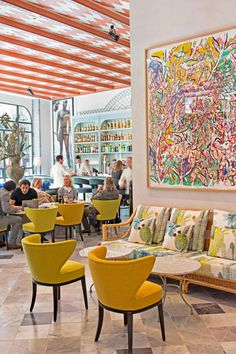 people sitting at tables in a restaurant with yellow chairs and artwork on the wall behind them