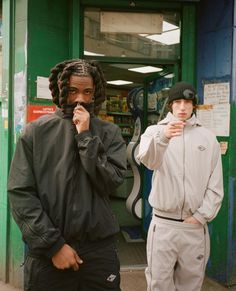 two young men standing next to each other in front of a green storefront door