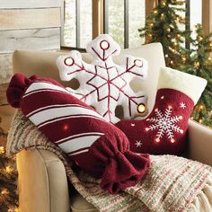 pillows and christmas decorations on a chair in front of a fireplace with snowflakes