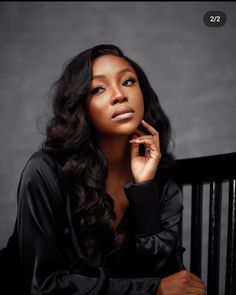 a woman with long hair sitting in a chair and posing for the camera, she has her hand on her chin