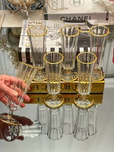 many glasses are lined up on a shelf in front of a chandelier with gold trimmings