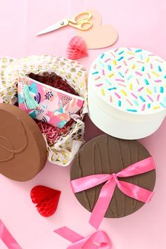 an assortment of treats and confetti on a pink surface with scissors, paper hearts, and ribbon