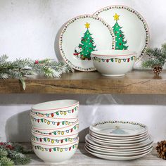 plates and bowls with christmas trees on them are sitting on a shelf next to pine cones