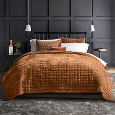 a bed with a brown comforter and pillows on it in front of a black wall