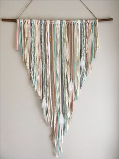 a wall hanging made out of different colored yarns and feathers on a wooden stick