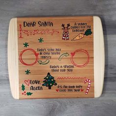 a wooden cutting board with christmas designs and words on the bottom, along with an ornament that says dear santa