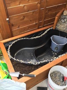 an outdoor bathtub with gravel in it and buckets on the ground next to it