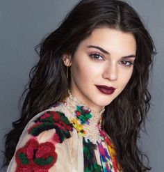 a woman with long dark hair wearing a colorful shirt and earrings, posing for the camera