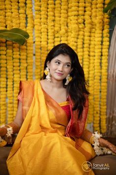 a woman sitting on the ground in front of yellow flowers and garlands with her hands behind her head