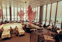 an indoor dining area with tables, chairs and potted trees in the center surrounded by large windows