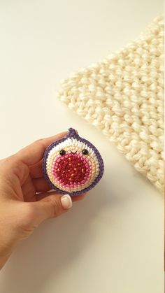 a hand holding a small crocheted object on top of a white table next to a pillow