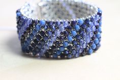 This layered bracelet was made by embellishing a netted base of Japanese seed beads with a mix of blue Swarovski crystals, glass pearls, and fire polished beads.   It's 7 1/4 inches long and 1 1/8 inch wide and closes with a silver toned magnetic slide clasp. Thanks so much for looking!! Elegant Blue Beaded Crystal Bracelet, Blue Beaded Bracelets With Spacer Beads For Party, Blue Beaded Crystal Bangle Bracelet, Blue Beaded Crystal Bracelet With Round Beads, Blue Beaded Crystal Bracelet, Blue Crystal Bracelet With Round Beads, Elegant Blue Crystal Bracelet With Polished Beads, Blue Beads With Bead Caps For Jewelry Making, Blue Crystal Beaded Bracelets For Jewelry Making