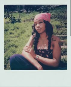 a woman sitting in the grass wearing a pink bandana and looking at the camera