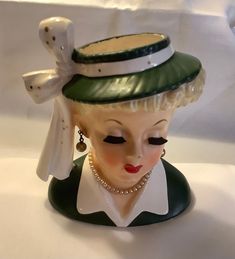 a ceramic figurine with a green hat and pearls on it's head