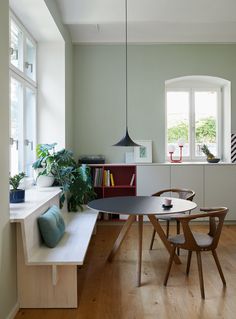 a dining room table and chairs in front of a window with potted plants on the windowsill