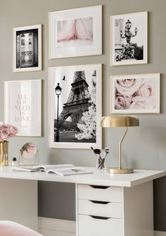 a white desk with pink flowers and pictures on the wall above it, along with a gold lamp