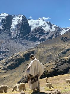 a man standing on top of a lush green hillside next to mountains covered in snow