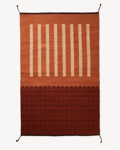 an orange and brown rug with white stripes on the top, in front of a white wall