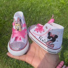 a person holding two pairs of shoes with minnie mouse on them, both in pink and white