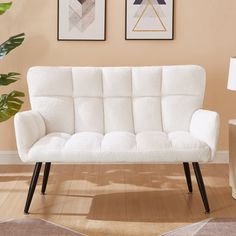 a white couch sitting on top of a hard wood floor next to a wall with two pictures above it