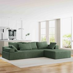 a living room with a large green couch and wooden floors in front of a kitchen