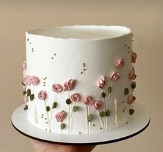 a hand holding a white cake with pink flowers on it