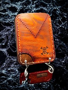 a leather case with a chain attached to it on a black surface and some water behind it