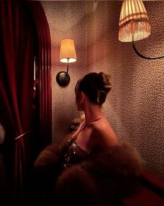 a woman sitting in front of a lamp next to a red wallpapered room