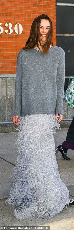 a woman with long hair walking down the street in a feathery skirt and sweater