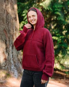 a woman in a red hoodie is standing by a tree and smiling at the camera