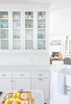 a kitchen with white cabinets and marble counter tops, along with lemons on a cutting board