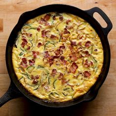 an omelet in a cast iron skillet on a wooden table with bacon and zucchini