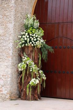 a tree stump with flowers and greenery on it in front of a wooden door